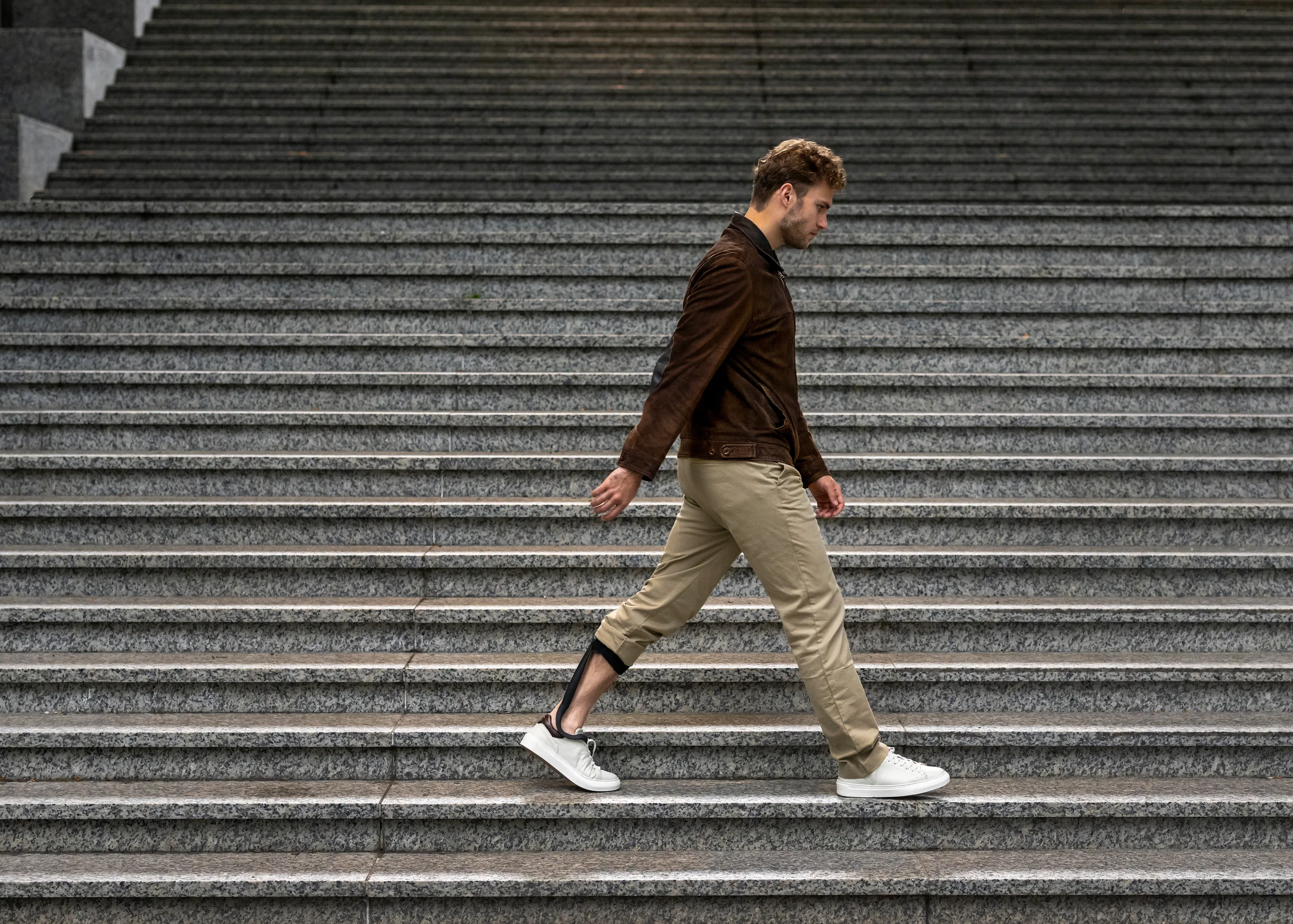 A man walking up stone steps wearing The Rise ankle-foot orthosis