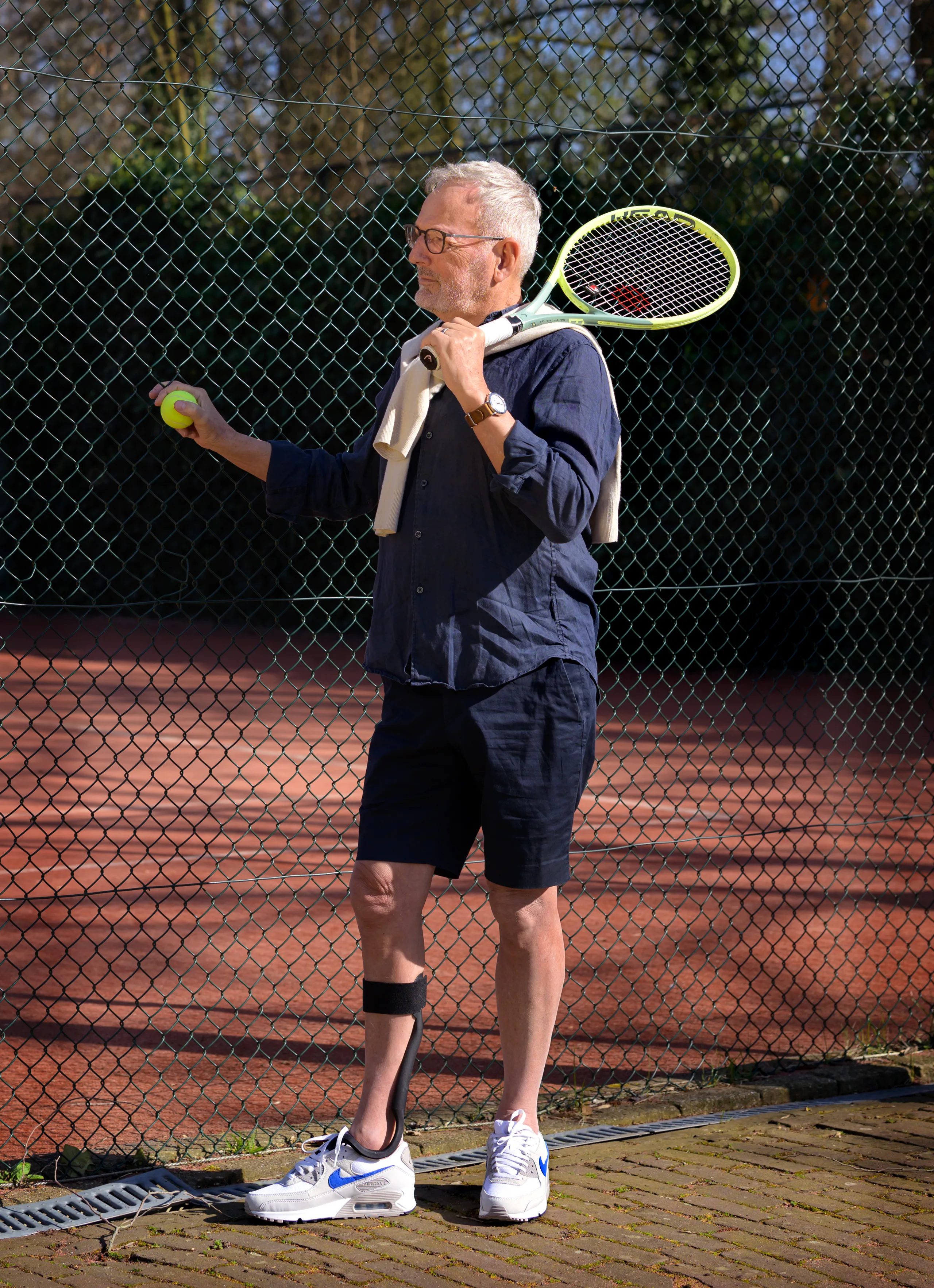 A man on a tennis court wearing The Rise, racket over shoulder
